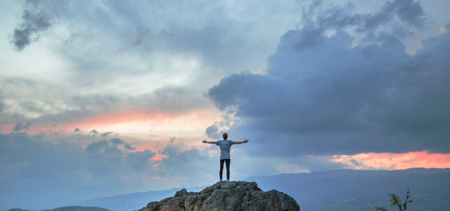 Man on top of mountains spreads arms in relief after IV ketamine treatment
