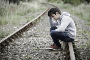 Can inflammation cause suicide? Young man sits on train tracks.